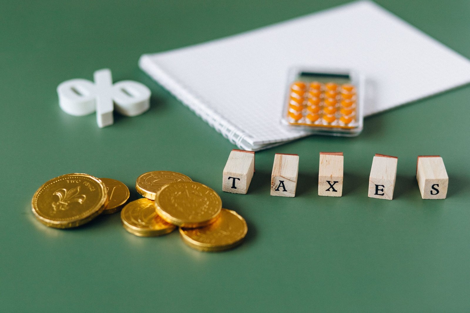 Gold coins, a percent sign and TAXES letter blocks on a green background